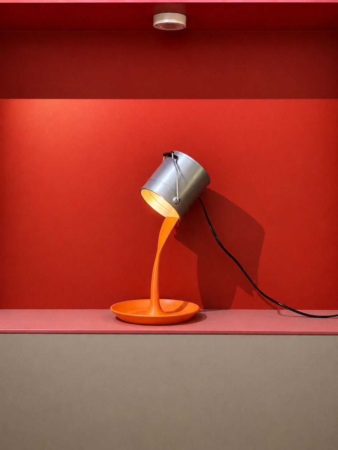 Spill — the paint-can lamp switched on, warm light glowing from inside the can onto the orange spill