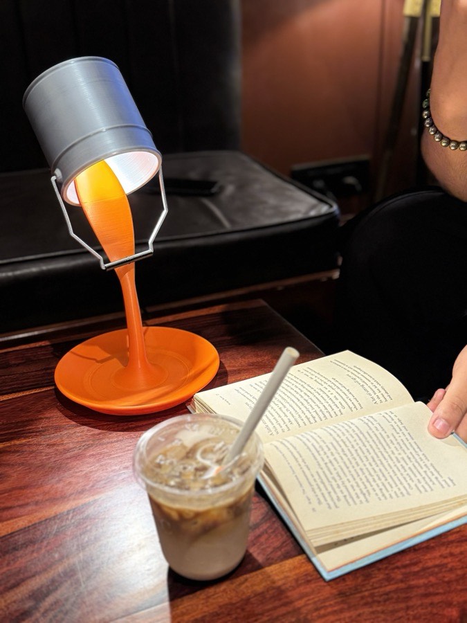 Spill lamp lit on a café table next to an open book and iced coffee